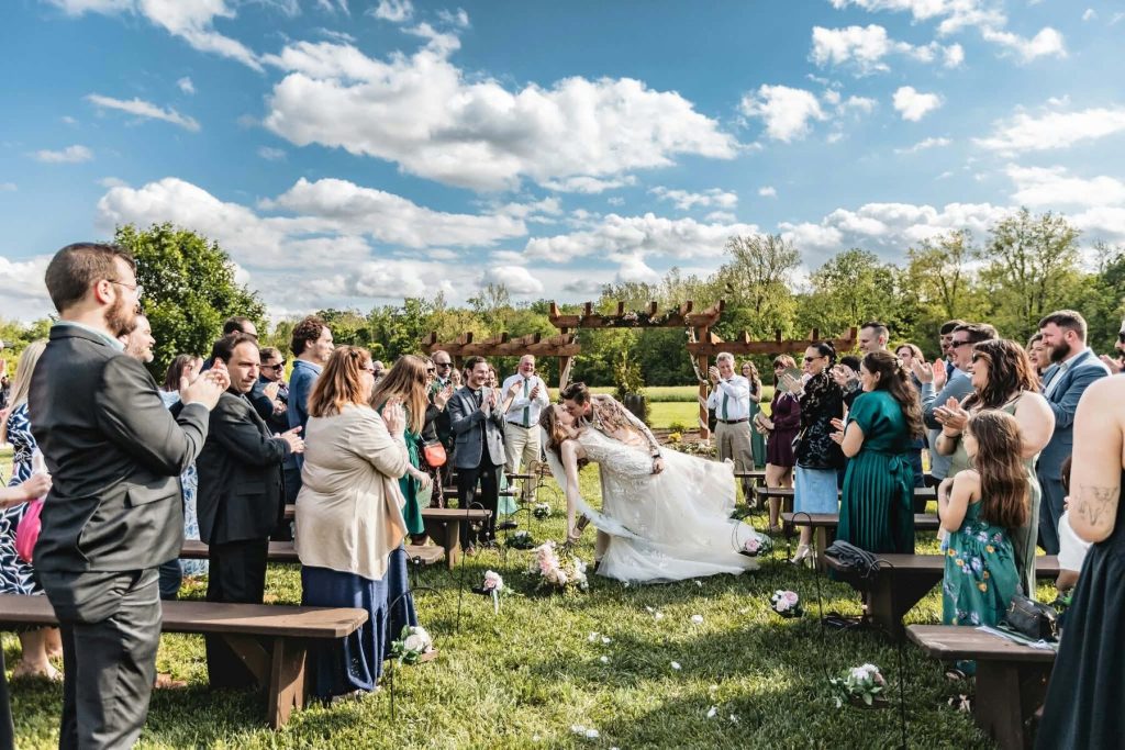 Newlyweds share a dip kiss as guests cheer at an outdoor Indiana wedding